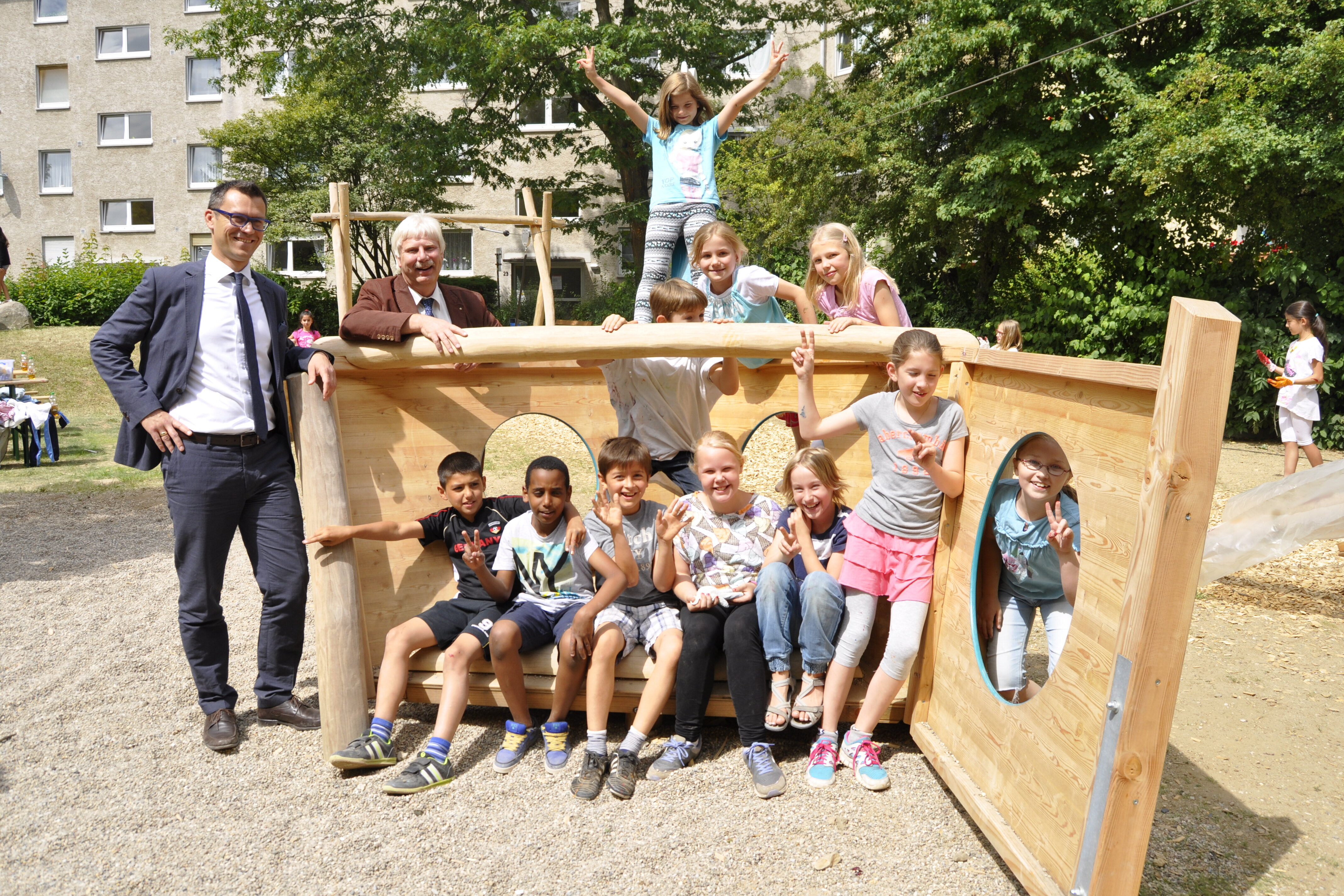 Vertreter der Stadt und HWB mit Kindern am neuen Kletterspielgerät aus Holz