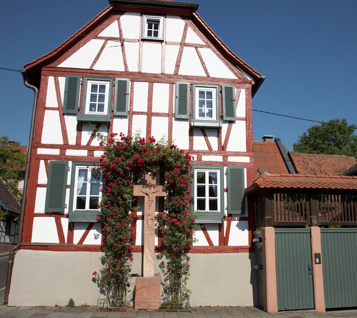 Blick auf ein Fachwerkhaus und von Rosen umranktes Kreuz