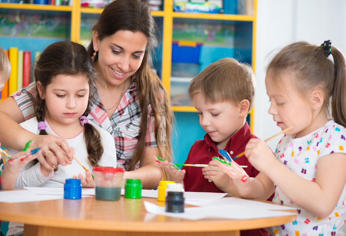 Frau sitzt am Tisch mit 3 Kindern und malt