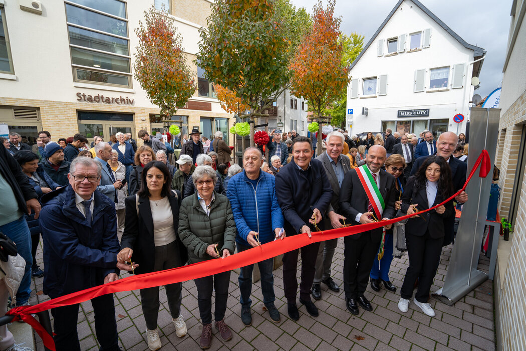 Stadtverordnetenvorsteher Andreas Hegeler (links), 1. Vorsitzende des Förderkreis Hofheimer Städtepartnerschaften Ingrid Bender (3. von links), Bürgermeister Christian Vogt (Mitte), Dezernent für Städtepartnerschaften Matthias Hees (5. von rechts), Buccinos Bürgermeister Pasquale Freda (4. von rechts) und Erster Stadtrat Daniel Phillip (rechts) mit Mitgliedern der Delegation aus Buccino beim Durschneiden des roten Bandes zur Eröffnung des Buccino Platzes.