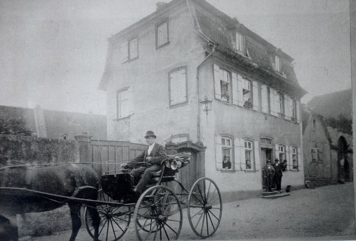 Schwarz-Weiß-Bild mit Kutscher im Vordergrund und Haus Löwenstein im Hintergrund, Wallau 1899